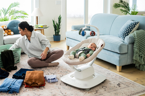 Bebé sobre la hamaca MamaRoo de Uppababy mientras la madre organiza en casa